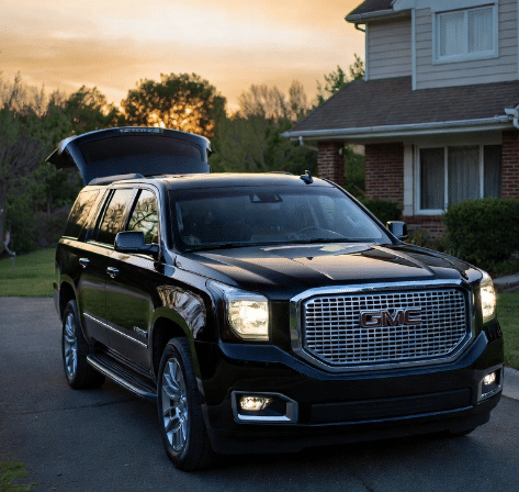 Front view of a black GMC Yukon Denali luxury SUV with an open trunk parked in a suburban driveway early morning for Airport Transfer