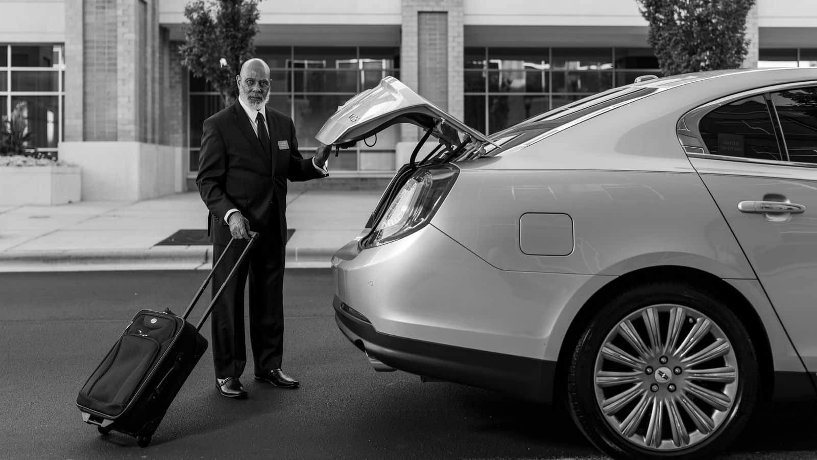 Chauffeur in a suit loading a suitcase into the trunk of a sedan before an airport ride
