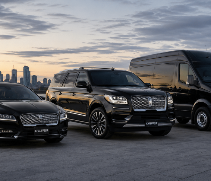 Three black luxury vehicles, including a Lincoln sedan, a luxury SUV, and a Mercedes Sprinter van, parked on a paved lot overlooking the Toronto skyline at sunset with the CN Tower visible